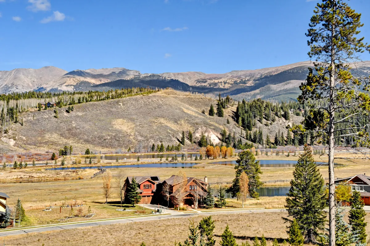 A tranquil exterior view showcasing majestic mountains, a shimmering lake, and charming homes nestled among trees. The scene invites guests to hike, fish, picnic, and take in breathtaking sunsets, emphasizing the outdoor appeal of the area.