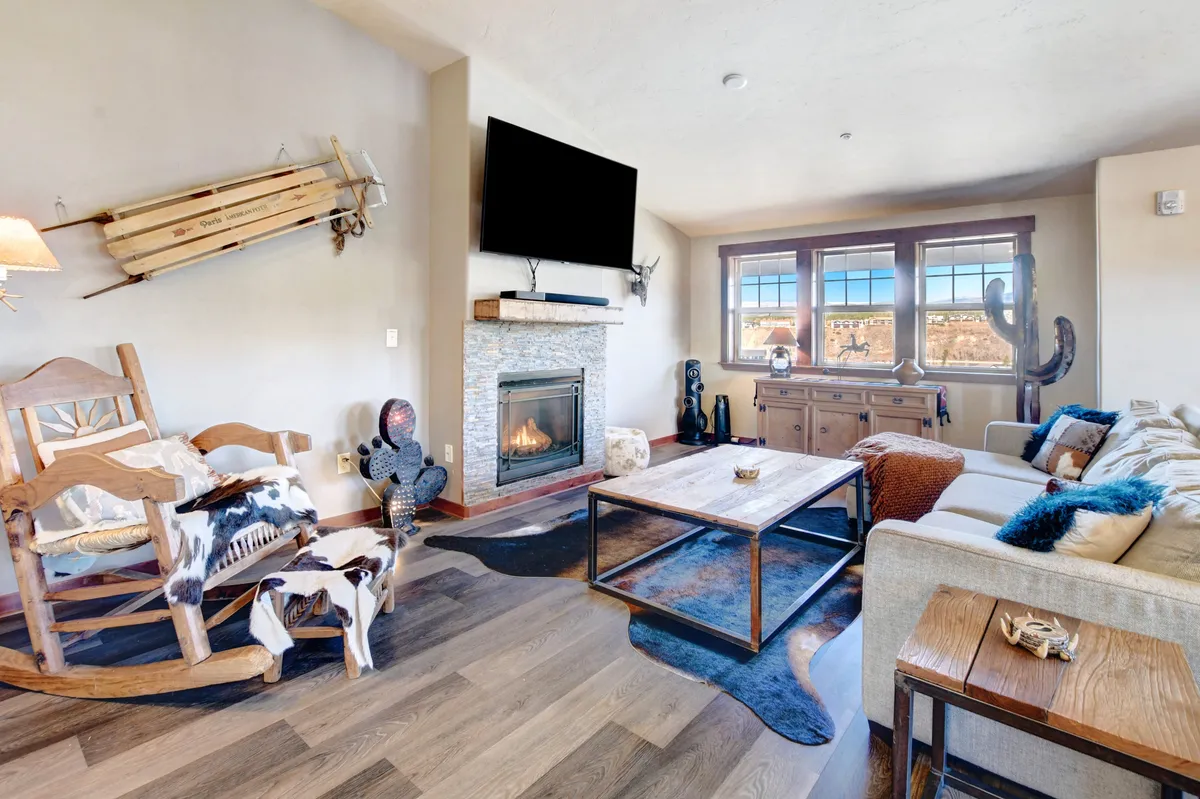 This image captures a warm and welcoming living room featuring a modern gas fireplace, plush sofa, rocking chair, and coffee table. The large windows let in ample natural light and offer scenic mountain views, creating a cozy gathering space ideal for relaxation after outdoor adventures.