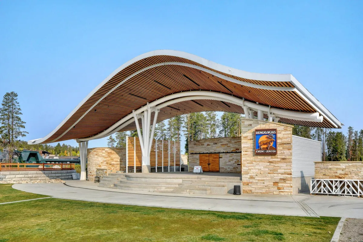An exterior view of a lively event space with a curved roof structure and stone walls, set up for community gatherings. Event signage and a festive crowd hint at concerts, festivals, and communal celebrations, all set against the backdrop of the resort's inviting atmosphere.