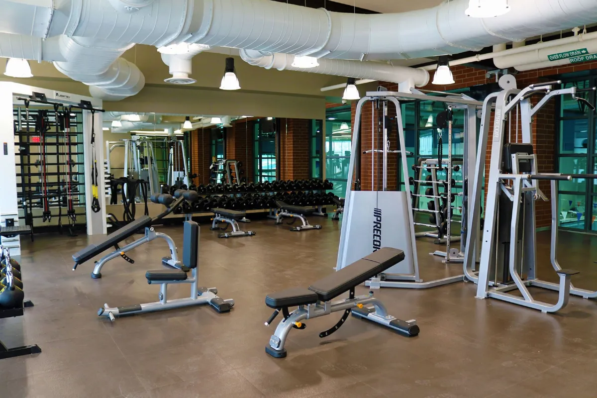 A modern, well-equipped gym with weight benches, a dumbbell rack, exercise machines, and mirrored walls. The space feels energizing and motivational, inviting guests to pursue their fitness goals or join group classes.