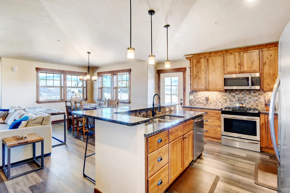 A stylish, open-concept kitchen and dining area showcasing a large island with bar seating, modern stainless steel appliances, and ample wood cabinetry. In the background, the dining area is seamlessly connected, emphasizing the inclusive and social layout perfect for both family meals and entertaining guests.