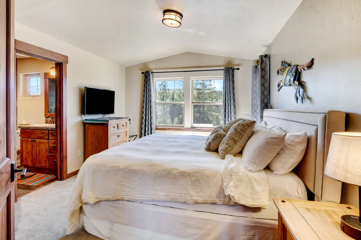 A serene bedroom featuring a cozy bed, window with a view, a decorative horse sculpture, a television, and a wooden dresser. The ambiance is calm and welcoming, ideal for unwinding after an adventurous day.