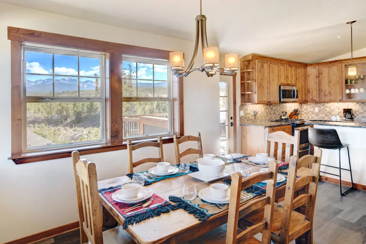 A cozy dining table positioned near the kitchen cabinetry, with a window framing a lovely mountain view. The setup invites natural light, creating a warm and inviting atmosphere ideal for family breakfasts or intimate dinners, further enhanced by the kitchen's proximity and accessibility.