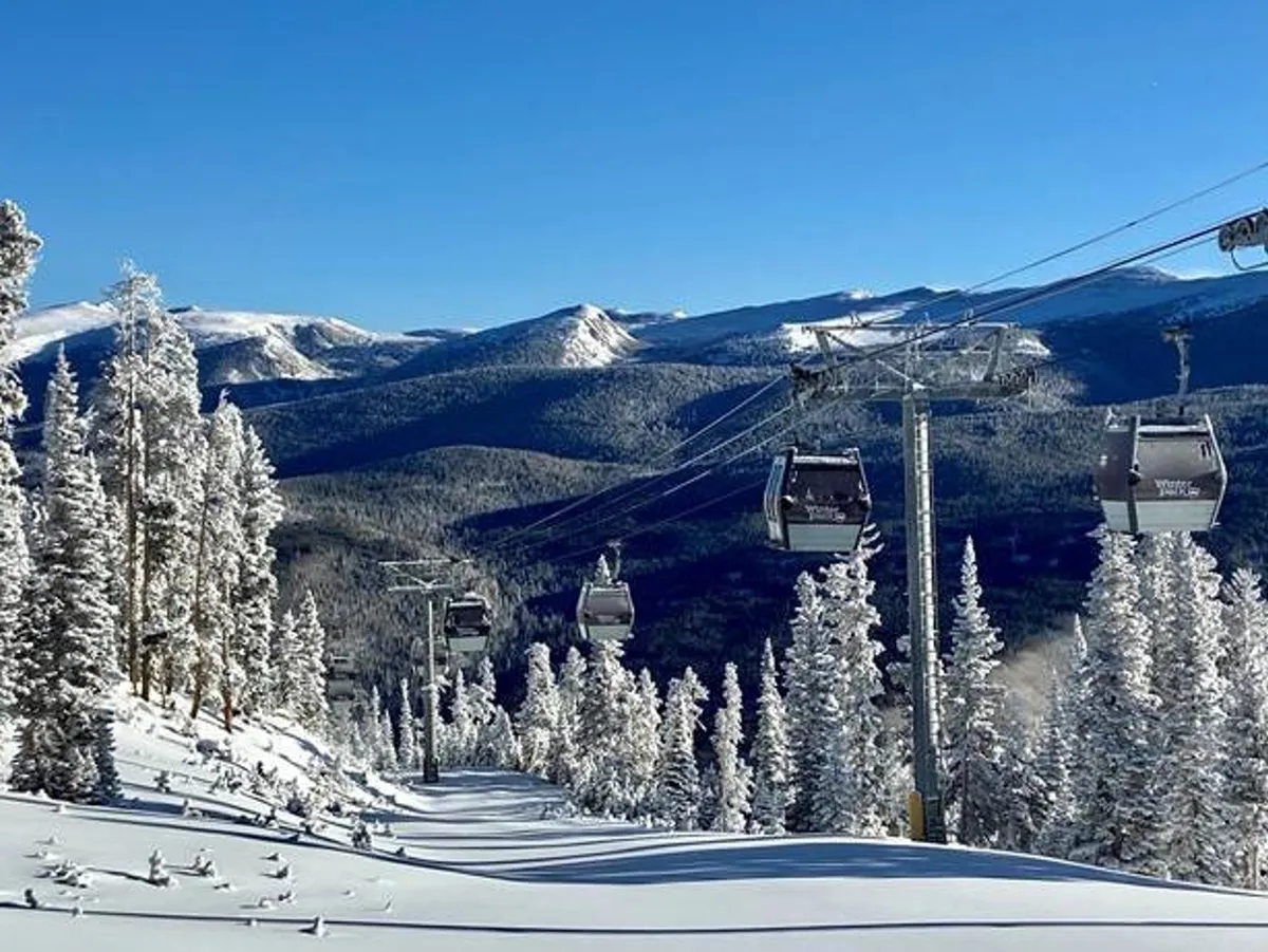 This image features ski lift gondolas against a backdrop of snow-covered trees and a majestic mountain range. The scene captures the excitement and serenity of winter sports in the Rockies, with panoramic views of the ski runs and inviting après-ski possibilities.