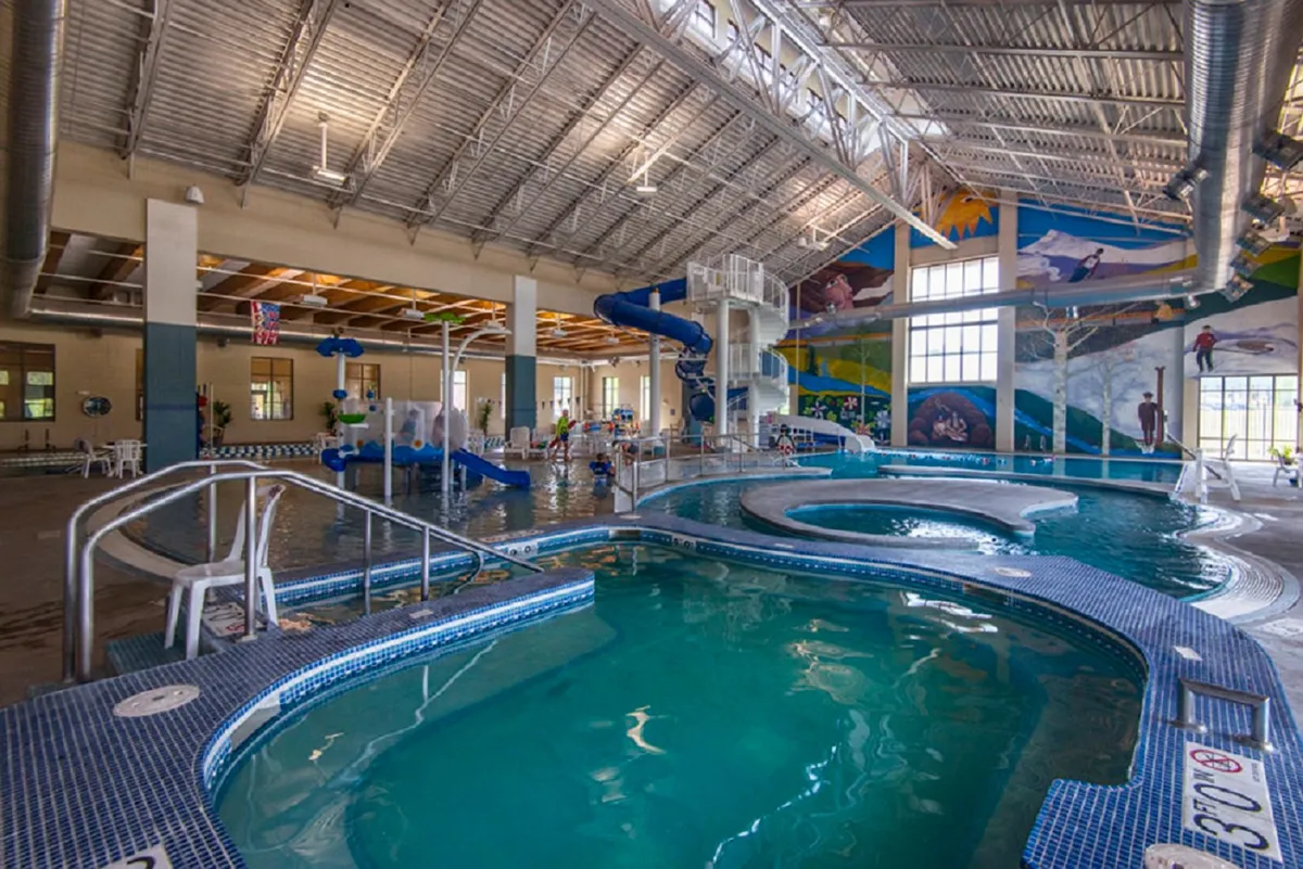 A vibrant indoor pool scene featuring colorful water slides, a spacious swimming area, and children playing joyfully. The environment is lively, with bright murals and open spaces perfect for families to enjoy aquatic activities together.