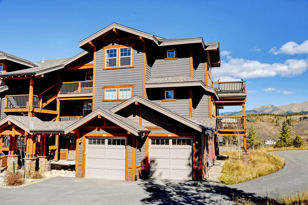 This exterior shot showcases the property’s inviting architecture, featuring wooden beams, expansive windows, and multiple balconies set amidst lush landscaping. The overall mood is warm and welcoming, with clear sightlines to mountain horizons that highlight the secluded, upscale atmosphere.