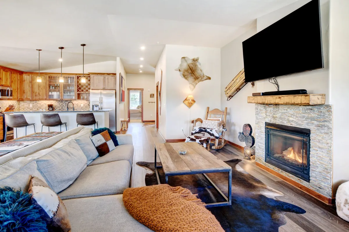 The image showcases a spacious open-concept living area with a plush sectional sofa arranged around a glowing fireplace, a stylish dining area ready for shared meals, and an inviting kitchen bar—perfect for gathering with family or friends. The space exudes warmth and comfort, hinting at cozy evenings and joyful celebrations.